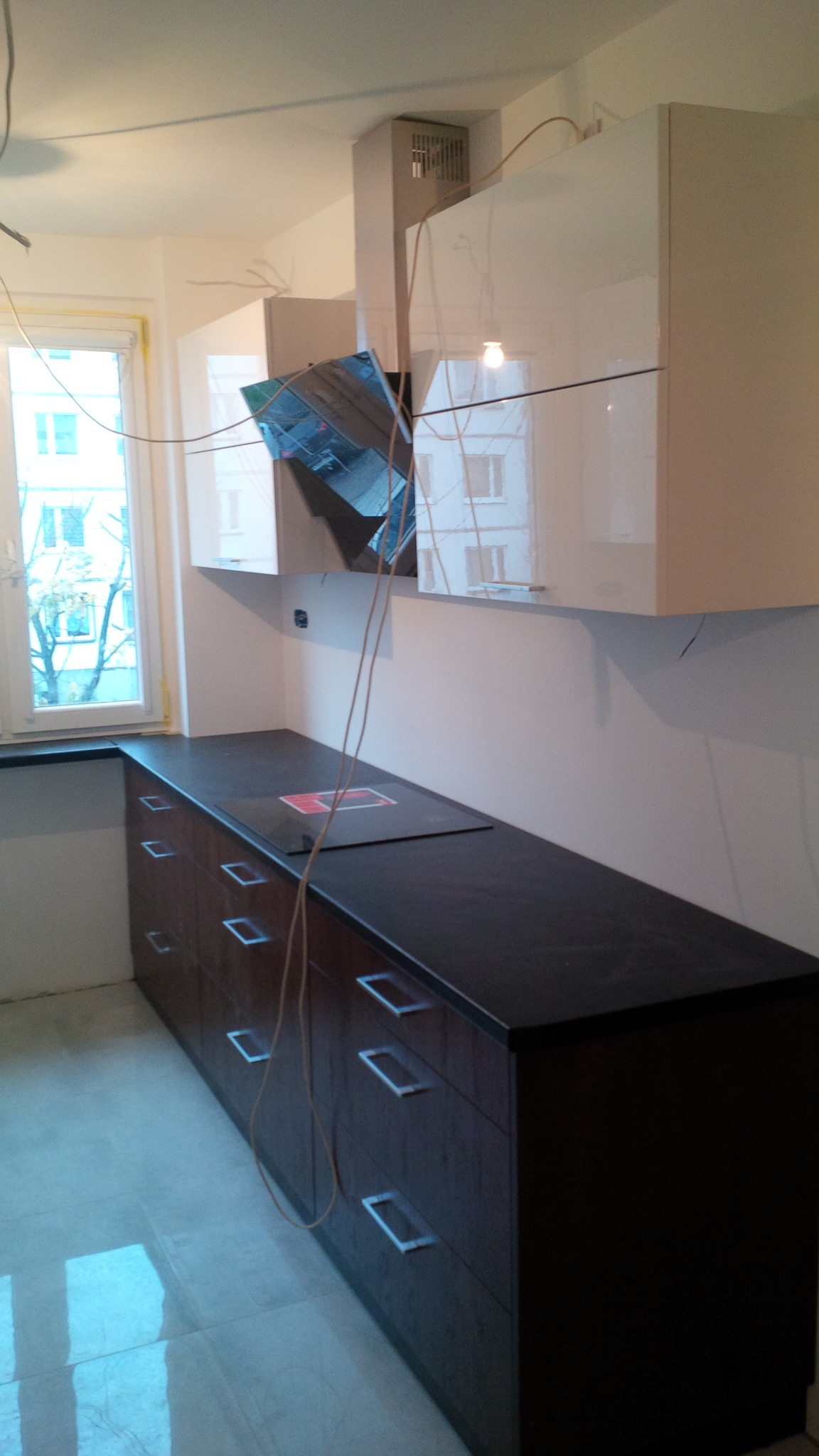 Montaż szafek kuchennych w Suwałkach w trakcie realizacji, widoczne podłączenia elektryczne, białe szafki wiszące i ciemne szafki dolne z szufladami.