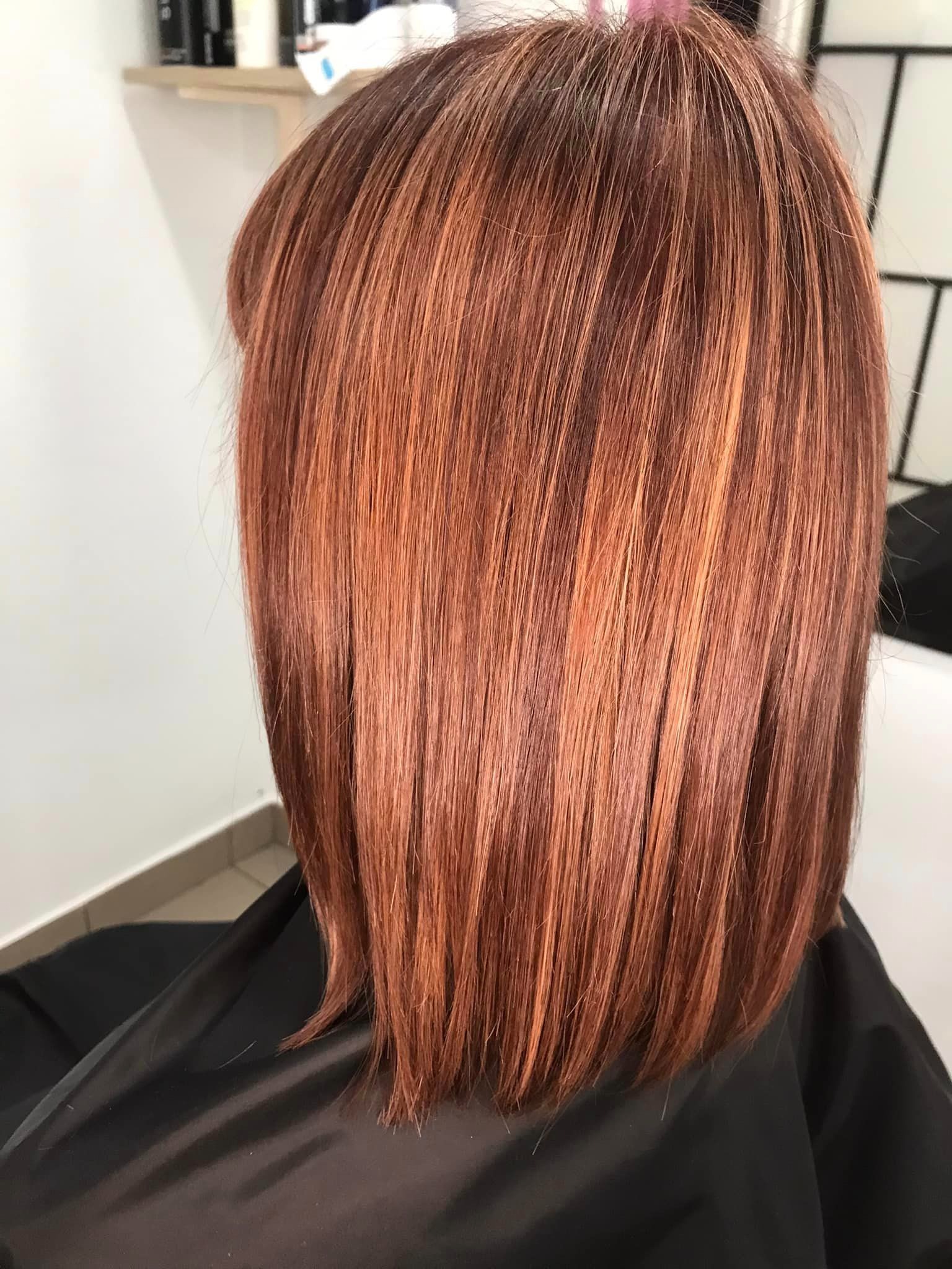 Ciemnorude włosy z refleksami w odcieniach blondu, ostrzyżone na boba, widoczne z tyłu na tle białej ściany salonu.