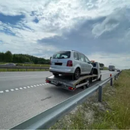 Srebrny samochód osobowy typu kombi przewożony na lawecie na autostradzie w słoneczny dzień.