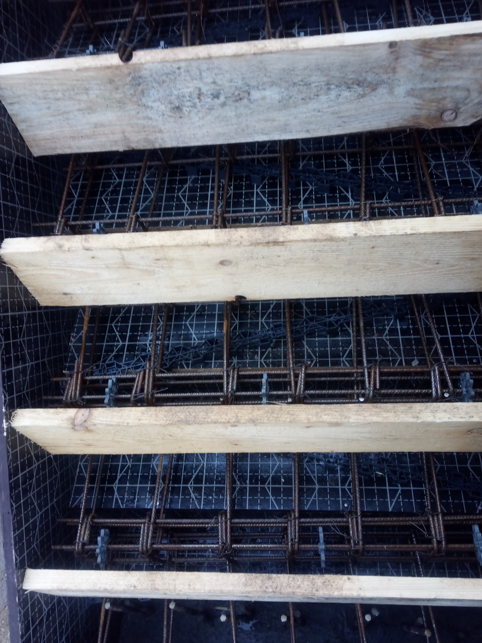 Zbrojenie fundamentu w szalunku z desek, widoczne elementy stalowe i siatka dystansowa.