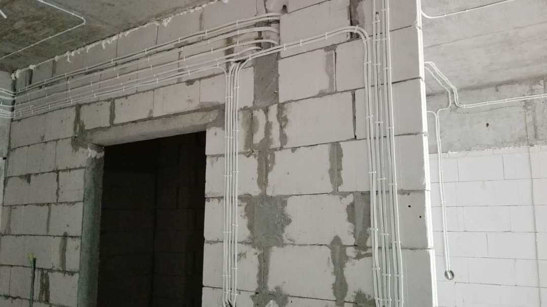 Białe przewody elektryczne ułożone w rurkach na surowych ścianach z betonu komórkowego w nowym budynku, widoczne mocowania przewodów.