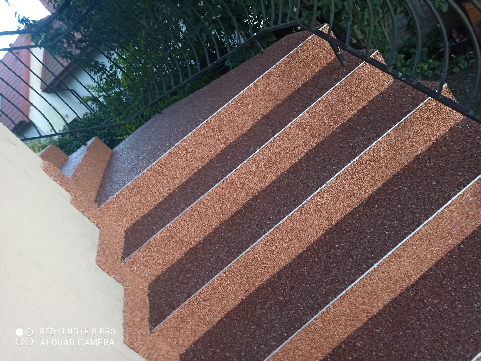 Wykończone schody zewnętrzne z żywicznej posadzki w odcieniach brązu, z metalową barierką, widok z góry.