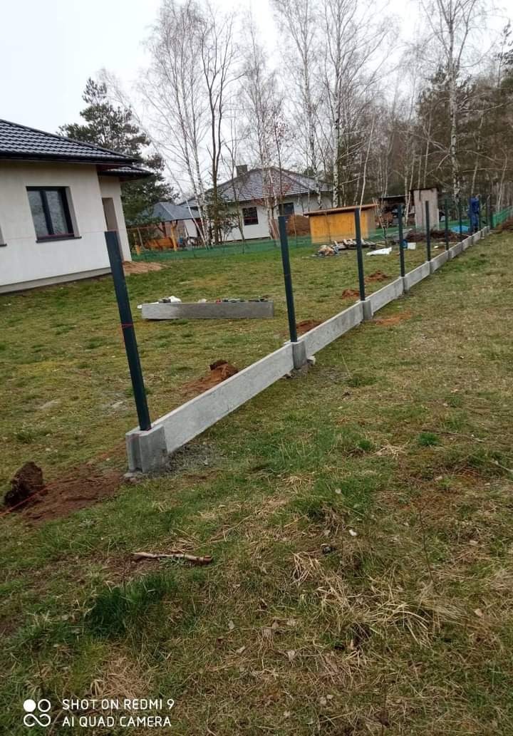 Montaż betonowej podmurówki i słupków metalowych pod ogrodzenie panelowe na trawiastym terenie, widoczny dom w tle.