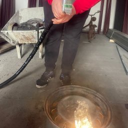 MK Laser - Obróbka metalowego elementu, prawdopodobnie felgi samochodowej, z użyciem urządzenia generującego intensywny strumień. Widoczne iskry i stopiony materiał wewnątrz felgi. W tle wózek budowlany...