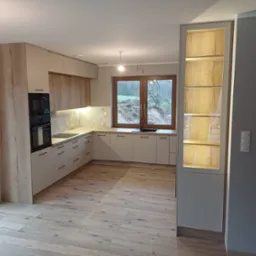 Jasna kuchnia w stylu skandynawskim z drewnianymi akcentami: fronty szafek z wyraźnym rysunkiem drewna, marmurowy backsplash, drewniana podłoga, okno z widokiem na zieleń, oświetlona witryna...