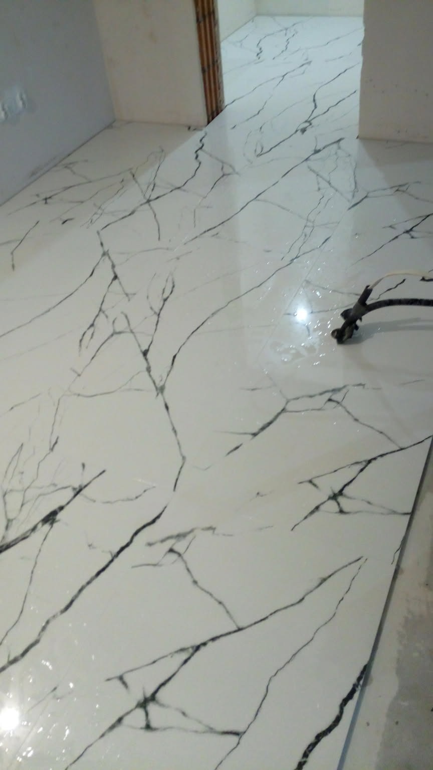 Błyszcząca, biała podłoga z czarnym wzorem marmuru, świeżo po ułożeniu. Widoczne narzędzie do rozprowadzania fugi i mokra powierzchnia. Ujęcie z niskiego kąta.