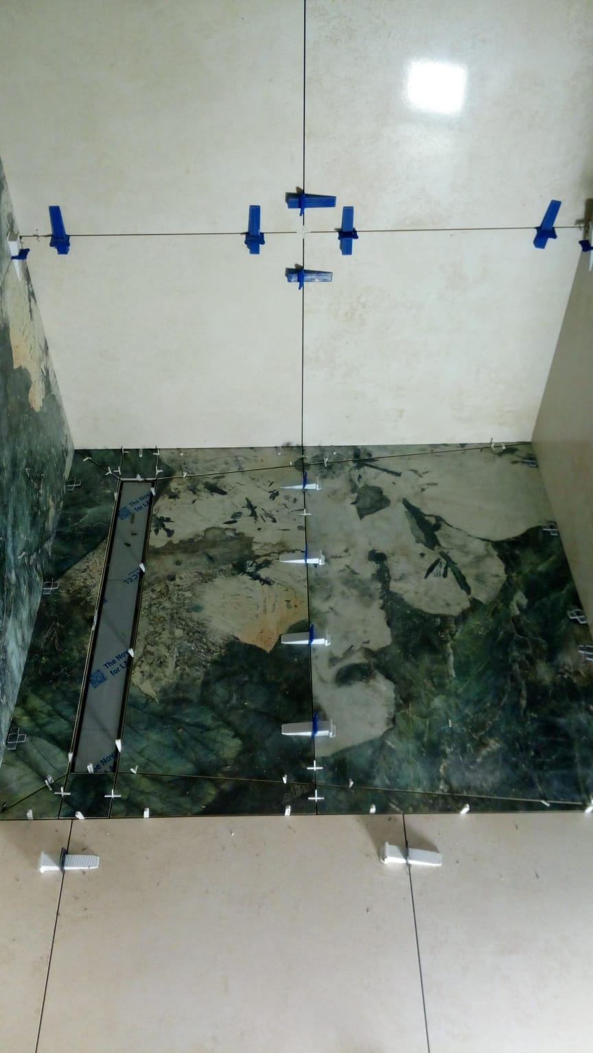 Układanie płytek podłogowych z zielonym wzorem, z użyciem niebieskich klipsów poziomujących. Widoczne fugi i fragmenty niezakończonej powierzchni.