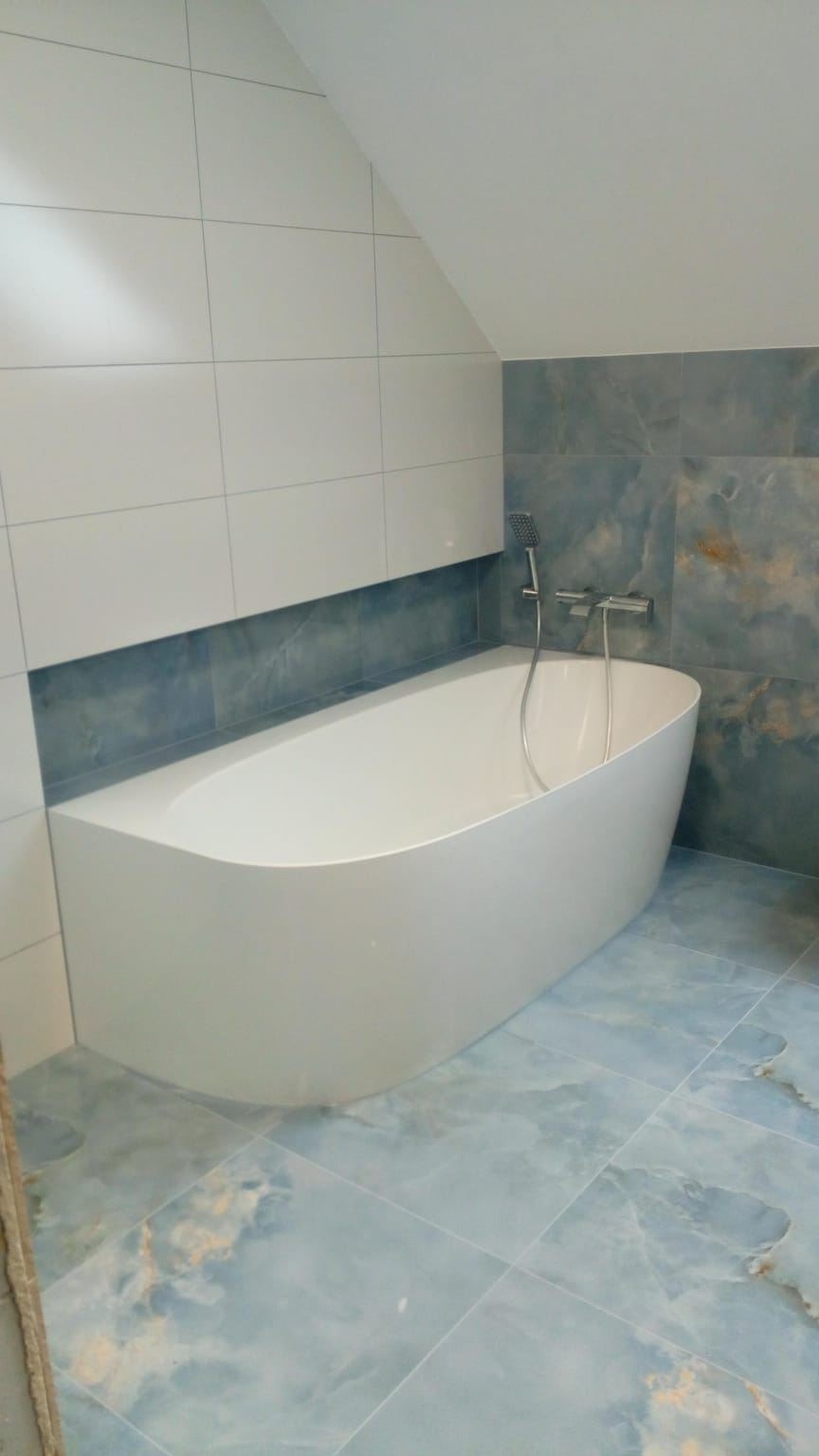 Nowoczesna łazienka na poddaszu z wolnostojącą wanną, biało-błękitnymi płytkami i minimalistyczną armaturą. Uwagę zwraca nietypowy układ płytek na ścianie.