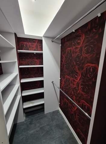 Wnętrze garderoby z białymi półkami i ścianą w bordowe róże, oświetlenie sufitowe, szara podłoga.