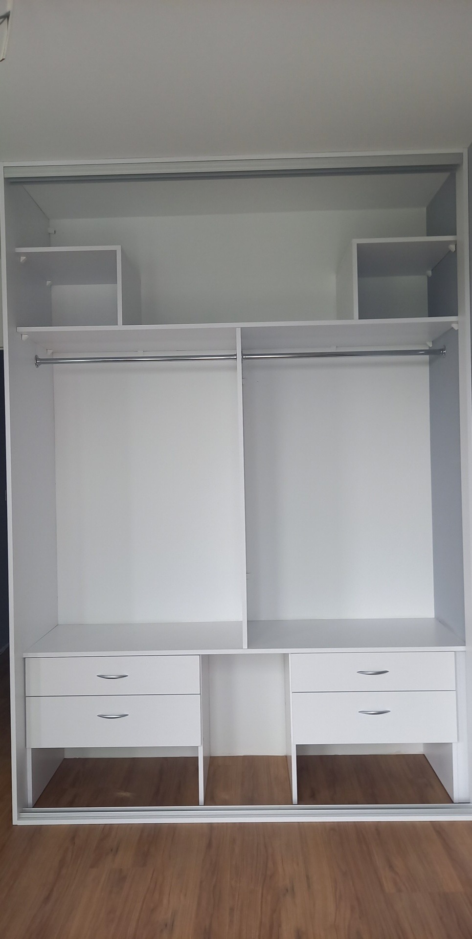 Wnętrze białej, przesuwnej szafy wnękowej z dwoma rzędami szuflad i półkami na górze, widok na puste przestrzenie do przechowywania.