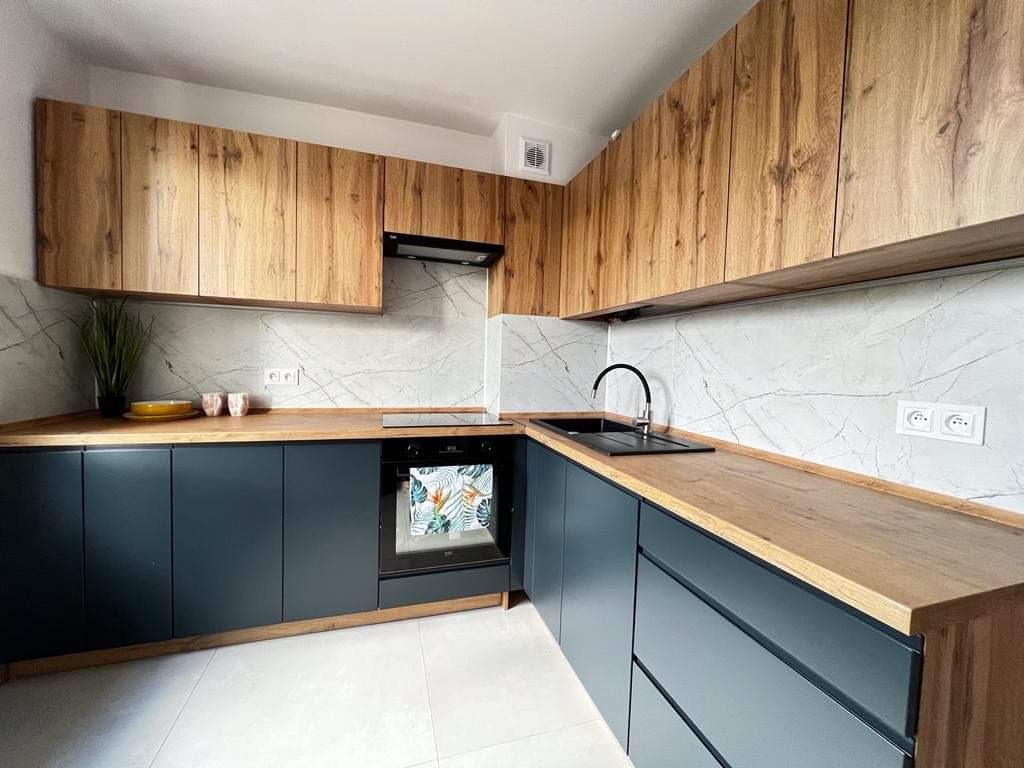 Nowoczesna kuchnia z górnymi szafkami z drewna o wyraźnym usłojeniu, dolnymi szafkami w kolorze grafitowym, marmurowym backsplashiem i drewnianym blatem.