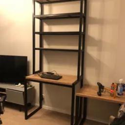 Metalowa konstrukcja regału z biurkiem z drewnianym blatem w nowoczesnym wnętrzu, widoczny laptop, narzędzia i napój.