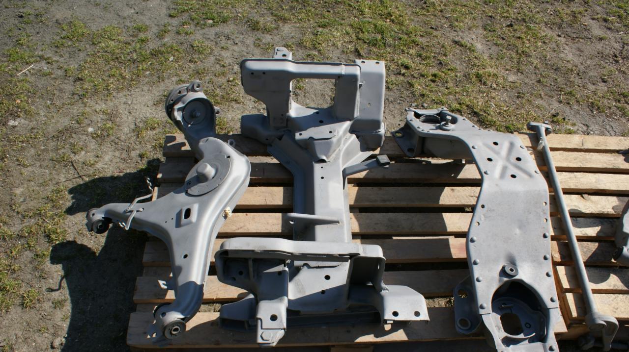 Elementy zawieszenia samochodowego po obróbce, leżące na drewnianej palecie na tle trawy.