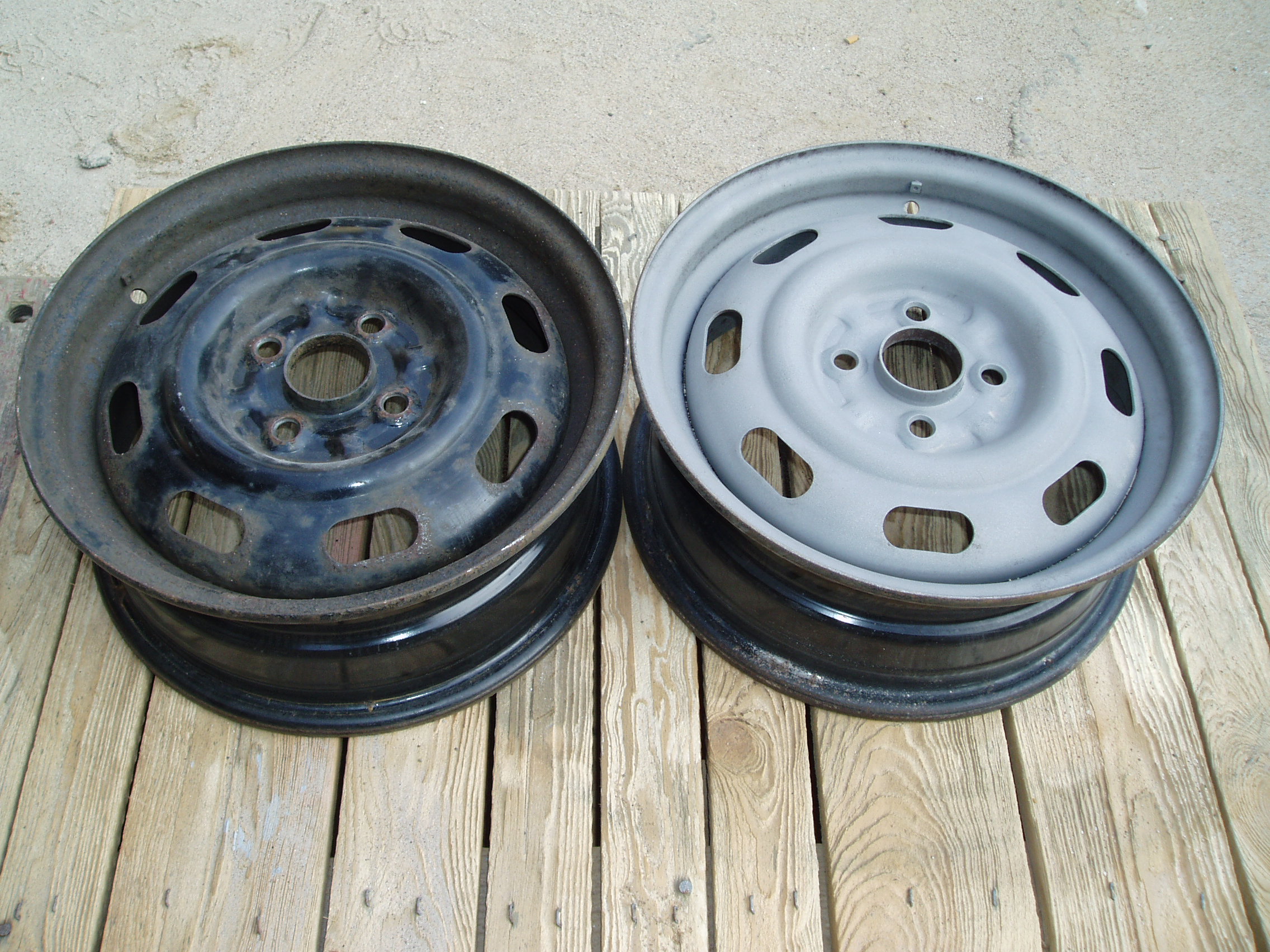Dwie felgi samochodowe na drewnianej powierzchni: jedna czarna, z widoczną rdzą i śladami użytkowania, druga szara, świeżo po oczyszczeniu i przygotowaniu do malowania.