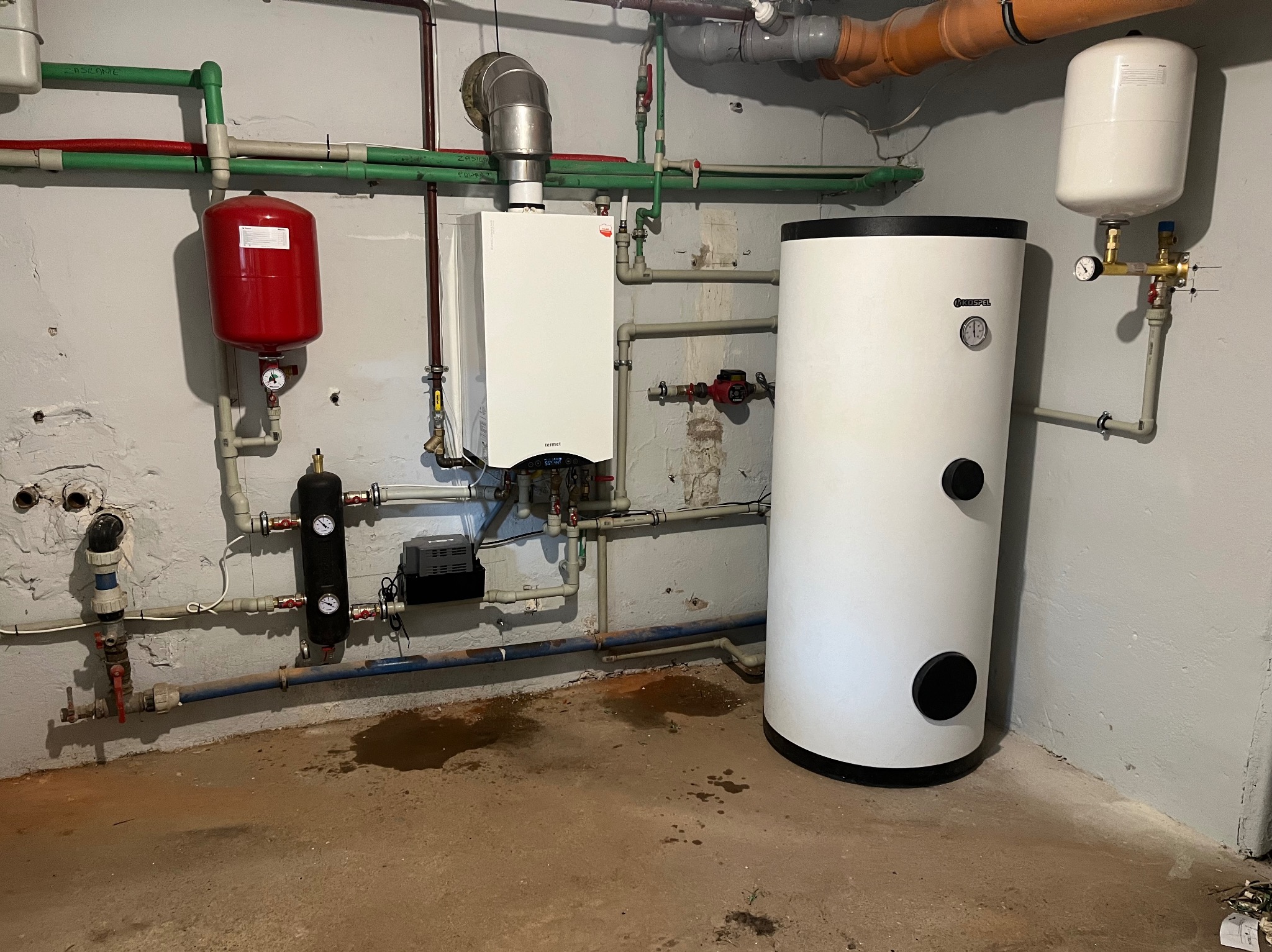 Biały piec gazowy Termet z podłączonymi rurami, obok biały zasobnik ciepłej wody Kospel, czerwony zbiornik przeponowy, instalacja w piwnicy.