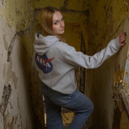 Wilku photography - Portret kobiety w bluzie z logo NASA, pozującej na zniszczonych schodach w opuszczonym budynku z odpadającą farbą.
