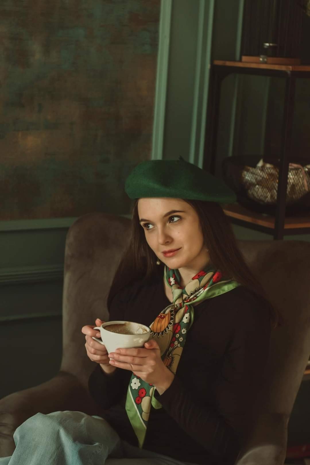 Portret kobiety w zielonym berecie, z wzorzystą apaszką, trzymającej filiżankę kawy w dłoniach, w studio fotograficznym w Szczecinie.