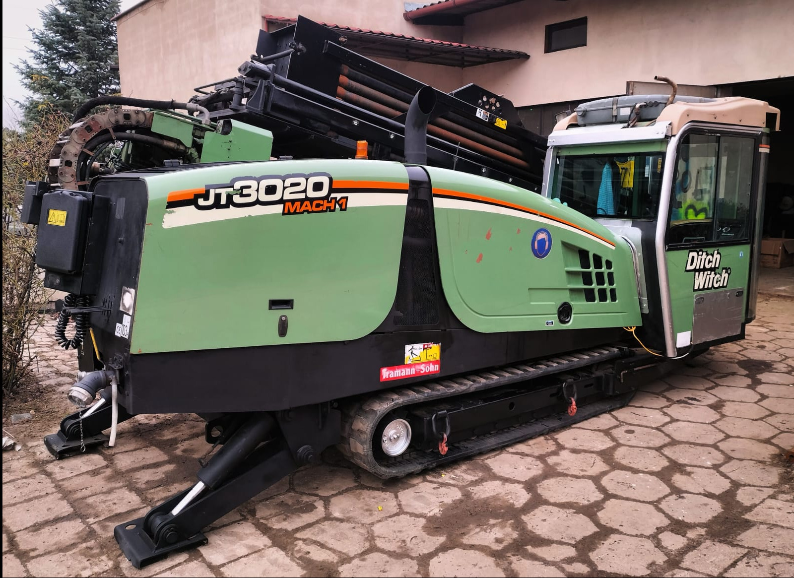 Wiertnica horyzontalna Ditch Witch JT3020 Mach 1 na gąsienicach, zaparkowana na kostce brukowej przed budynkiem.
