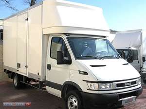 Biały samochód dostawczy Iveco z zabudową kontenerową, widoczny z boku, zaparkowany na zewnątrz. W tle drugi, podobny pojazd.