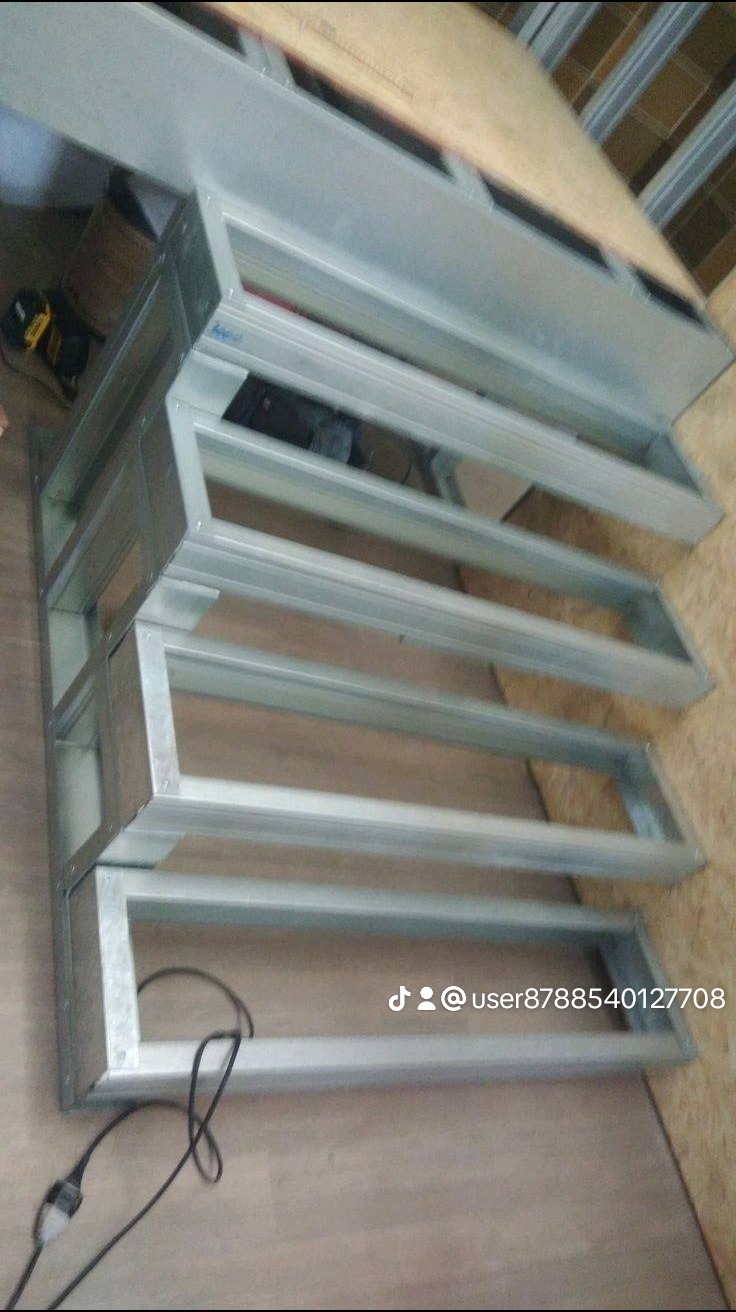 Metalowa konstrukcja schodów z profili zamkniętych, widoczne spawy, niedokończony montaż, przewody elektryczne w tle.