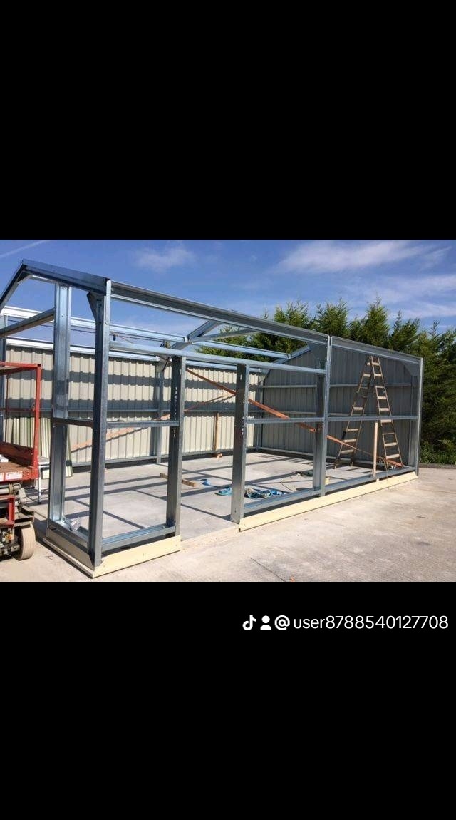 Konstrukcja szkieletowa z metalowych profili, prawdopodobnie garażu lub wiaty, w trakcie montażu, z widoczną drabiną opartą o ścianę szkieletu i wózkiem transportowym w tle.