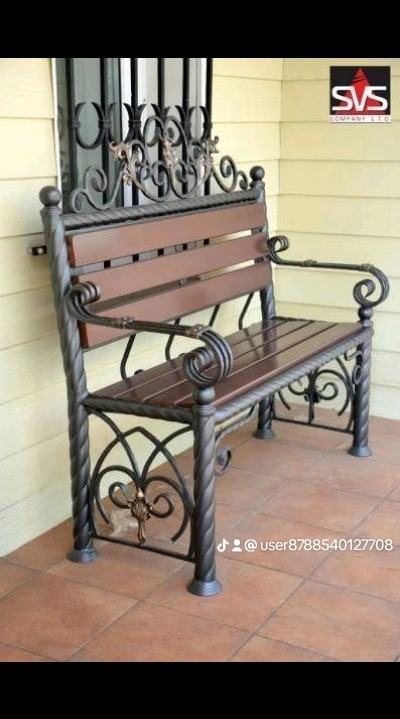 Kute żelazo i drewno tworzą dekoracyjną ławkę ogrodową na tarasie z terakoty, z logo firmy w prawym górnym rogu.