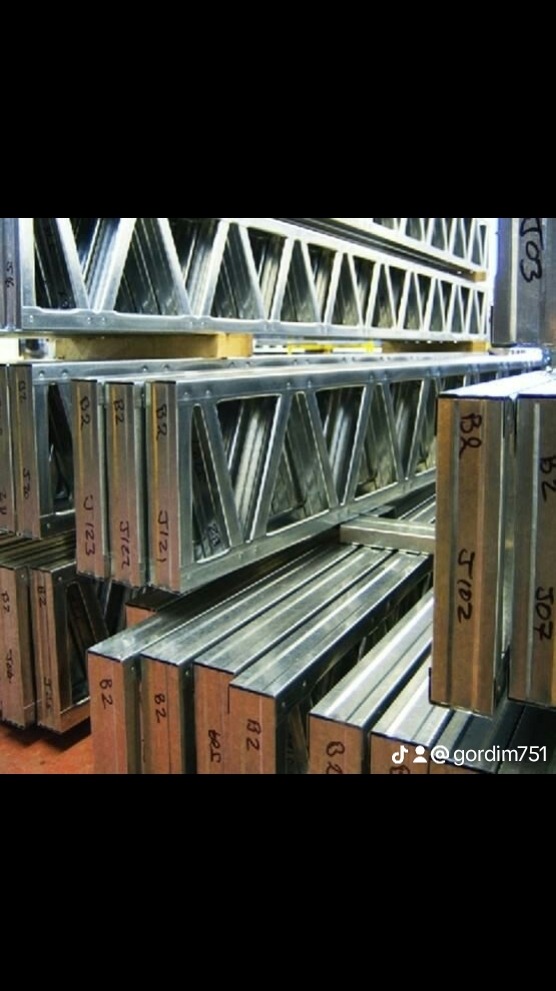 Stalowe kratownice konstrukcyjne, ułożone w stos, z widocznymi oznaczeniami numerycznymi i literowymi.