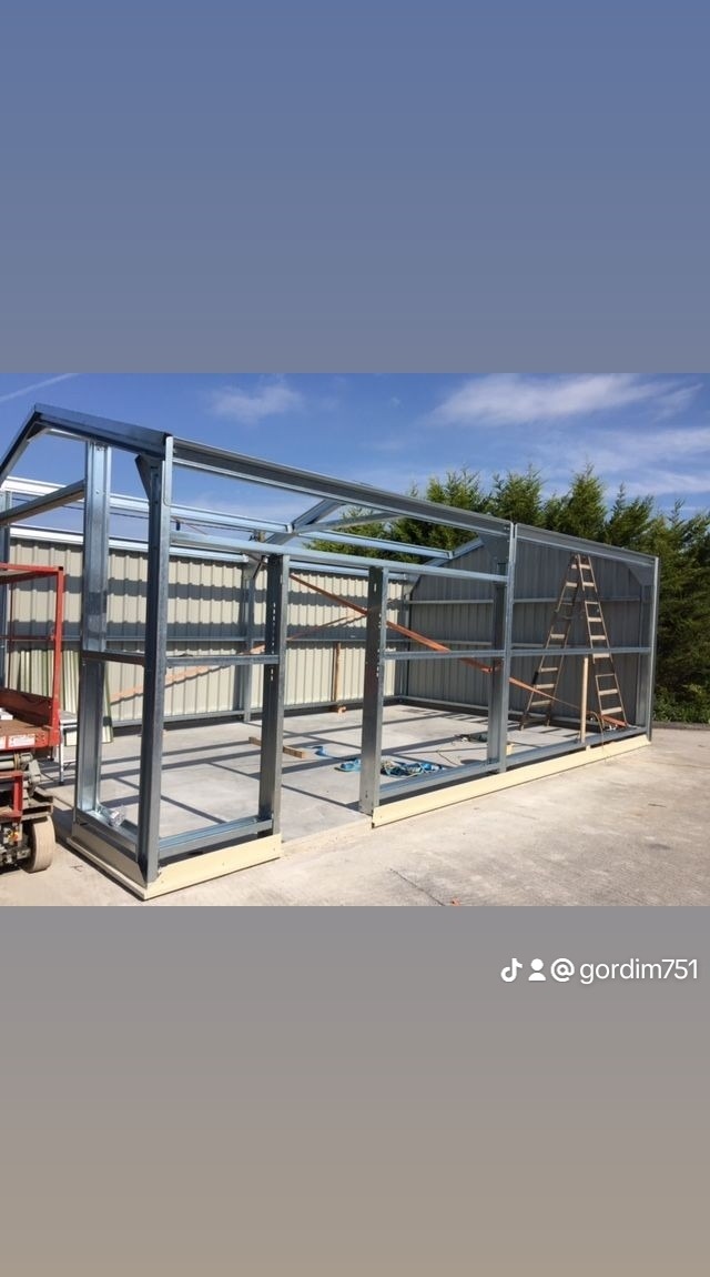 Konstrukcja szkieletowa budynku gospodarczego z profili stalowych, częściowo obłożona blachą trapezową, z widoczną drabiną opartą o ścianę szczytową i podnośnikiem koszowym z boku.