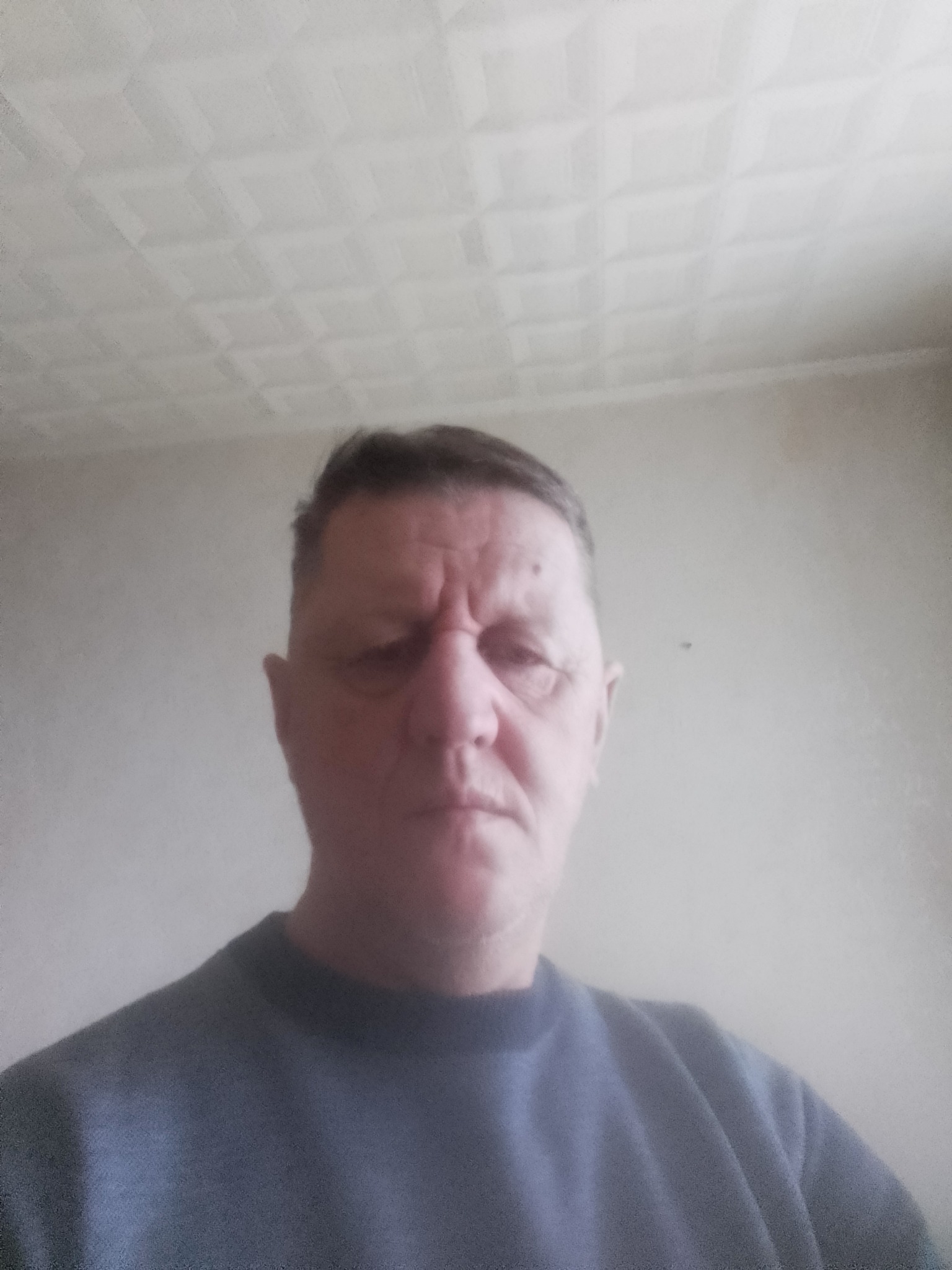 Portret mężczyzny w szarej bluzie na tle białego sufitu z kasetonami.