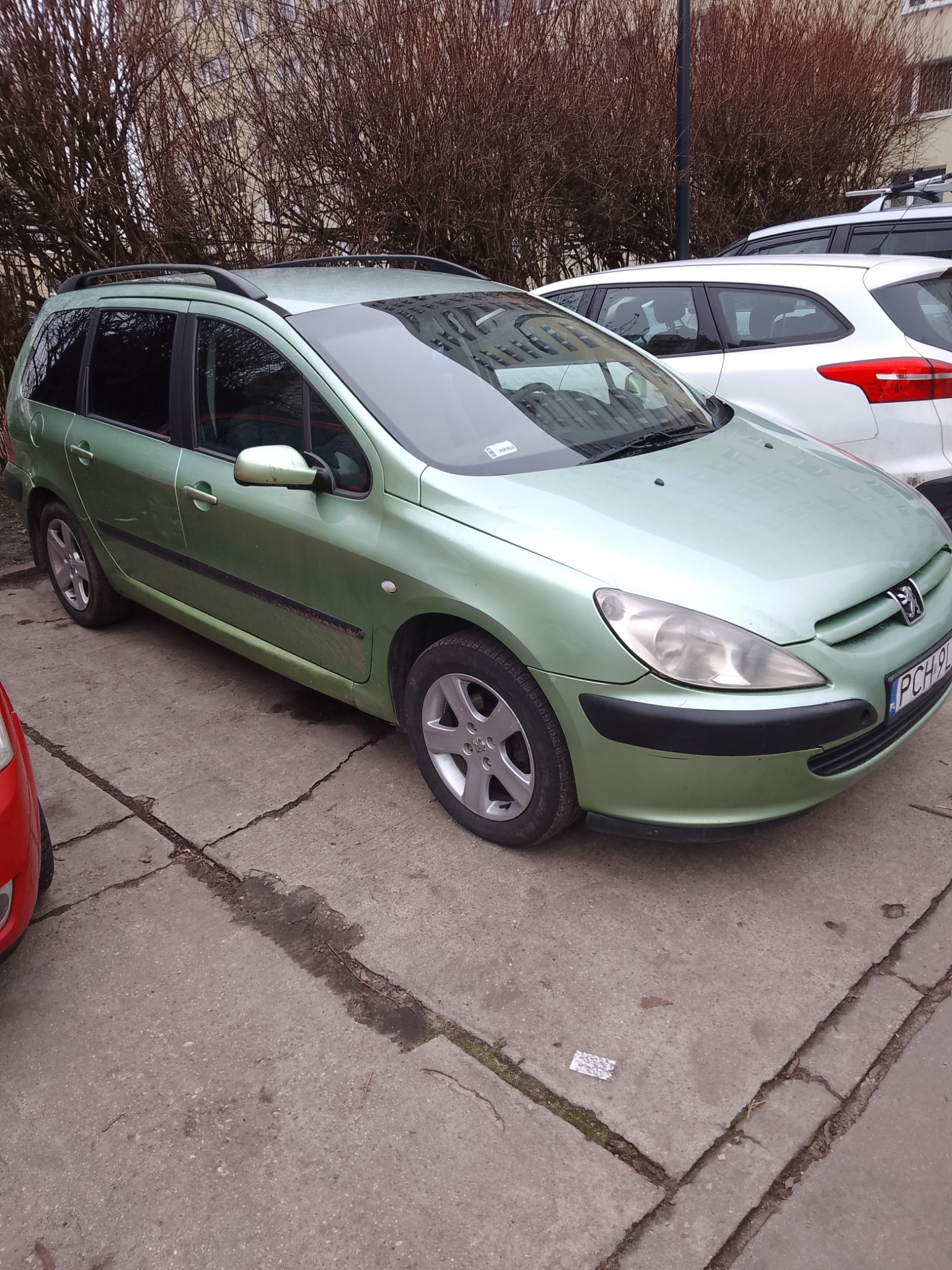 Jasnozielony Peugeot kombi zaparkowany na betonowym placu, widoczne relingi dachowe i tablica rejestracyjna PCH 9L.