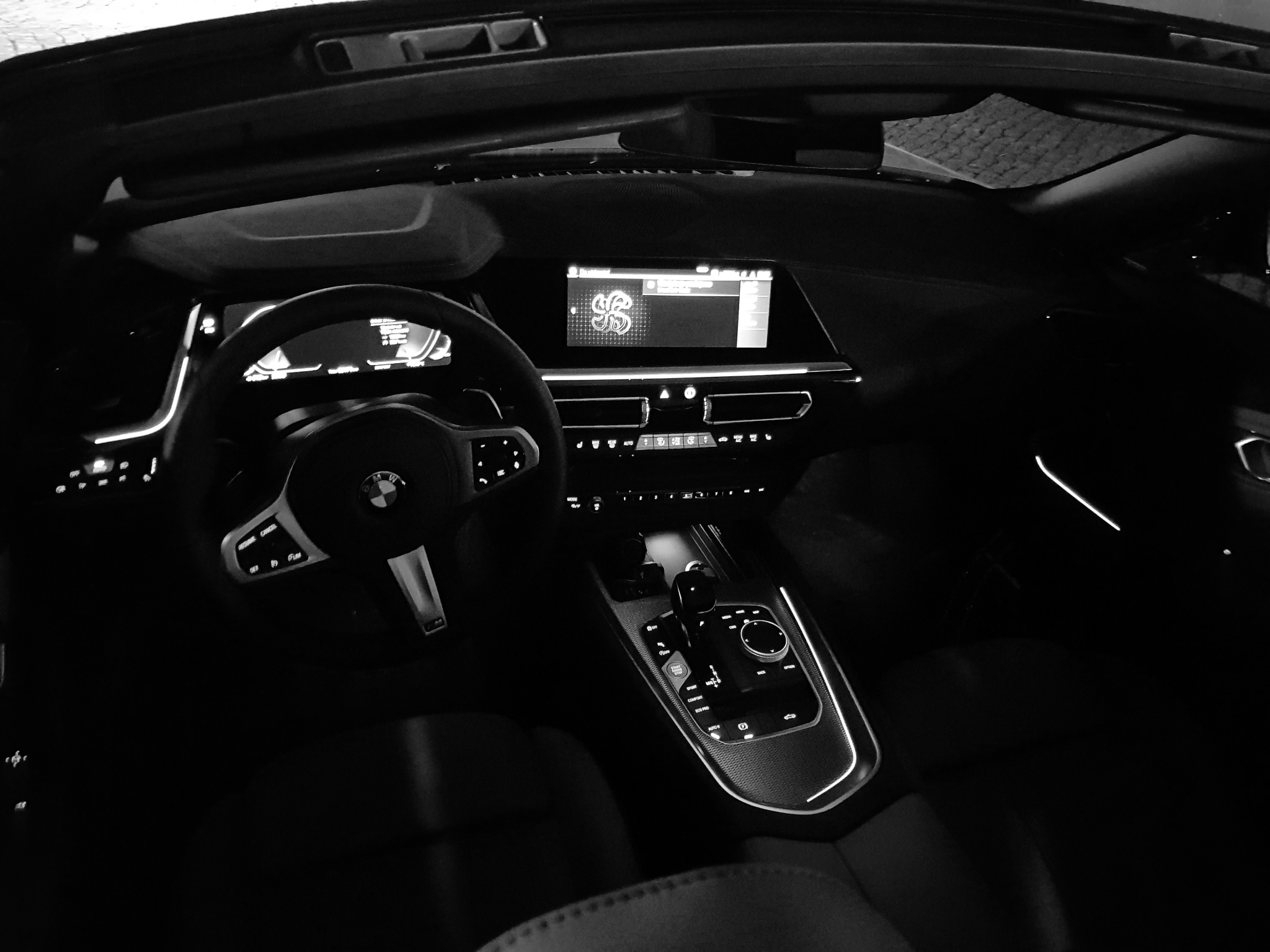 Wnętrze BMW Z4 z otwartym dachem, widok na deskę rozdzielczą, kierownicę z logo BMW i panel sterowania skrzynią biegów w czarno-białej tonacji.