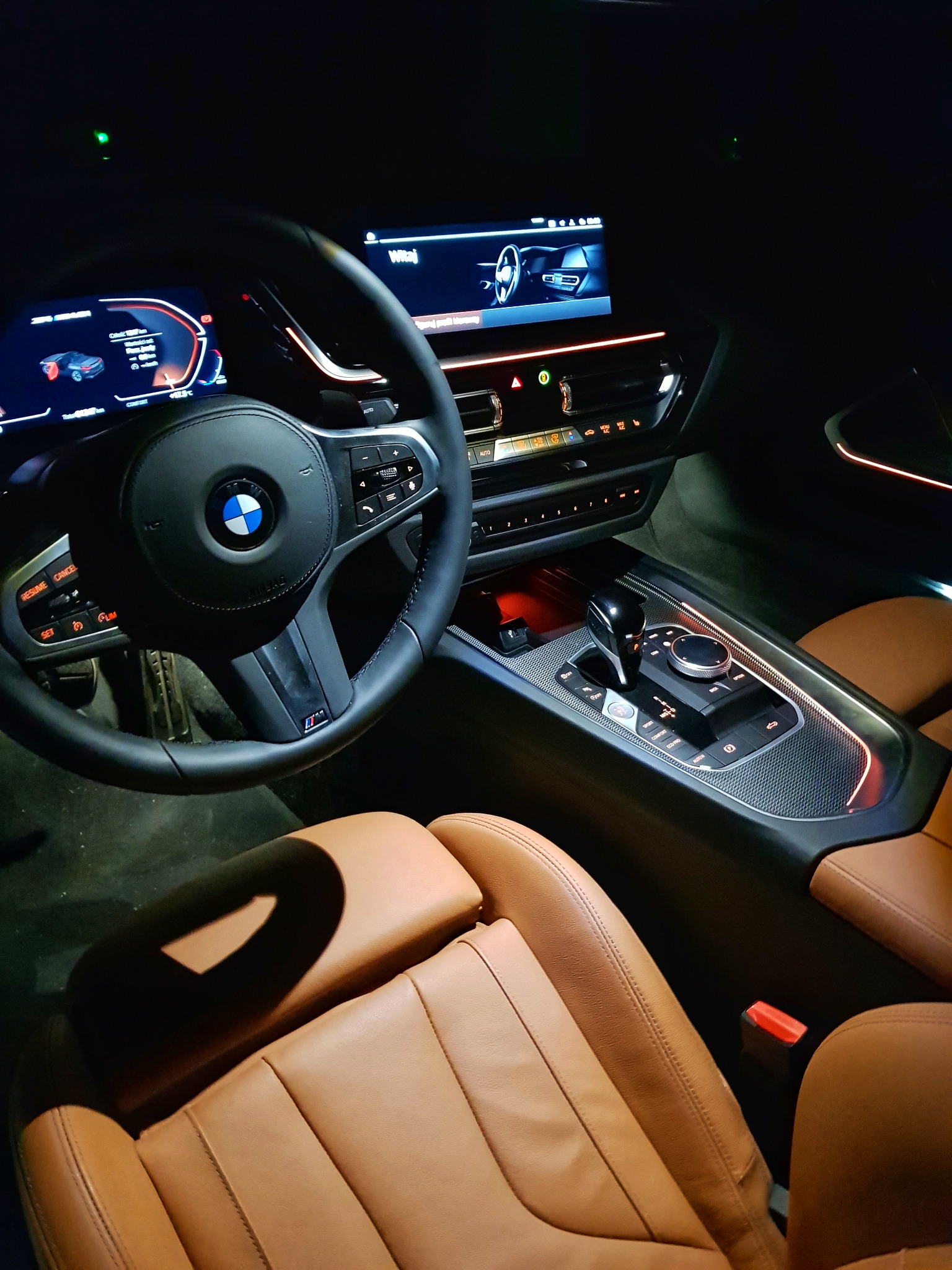 Wnętrze samochodu BMW Z4 z brązowymi skórzanymi siedzeniami, podświetleniem ambientowym i widocznymi ekranami deski rozdzielczej.