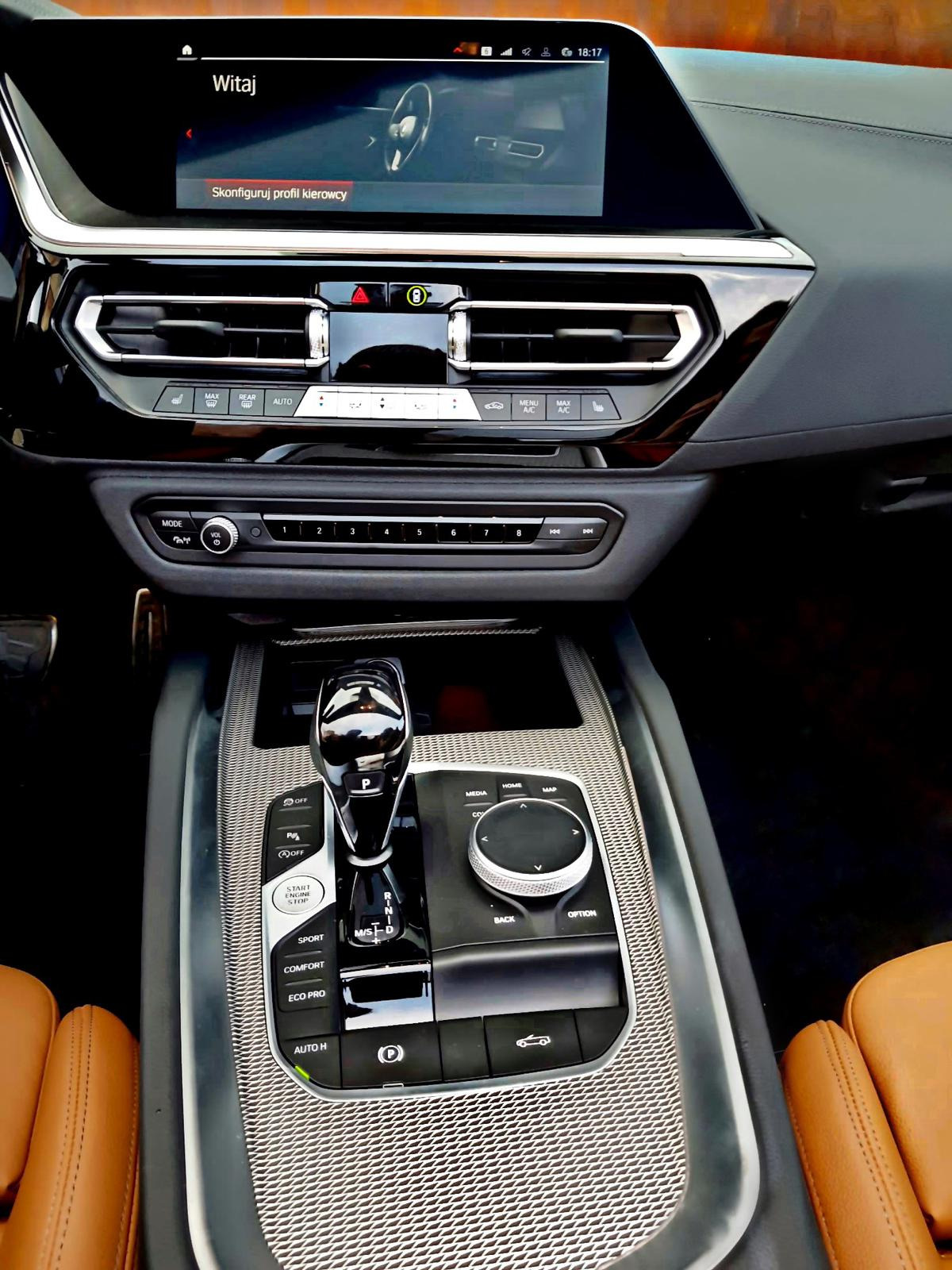 Wnętrze samochodu z widocznym kokpitem, ekranem dotykowym z komunikatem powitalnym i konsolą środkową z dźwignią zmiany biegów w pozycji parkowania.