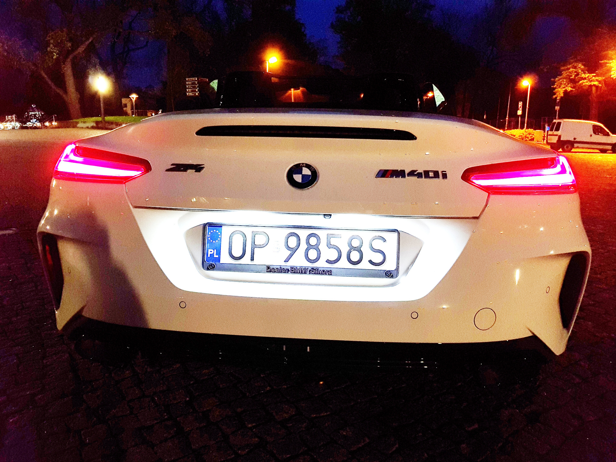 Białe BMW Z4 M40i, widok z tyłu w nocy, z widocznymi światłami i tablicą rejestracyjną z dealerem BMW Sikora.