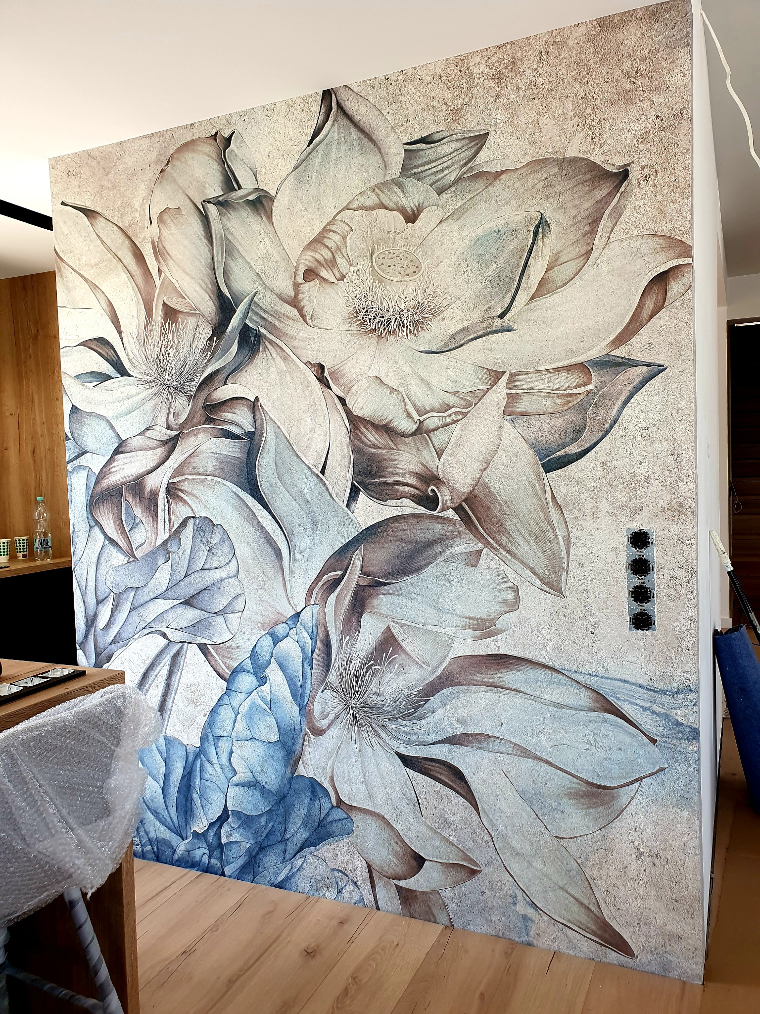 Ściana z fototapetą przedstawiającą kwiaty magnolii w odcieniach beżu i błękitu, z widocznymi gniazdkami elektrycznymi na ścianie.