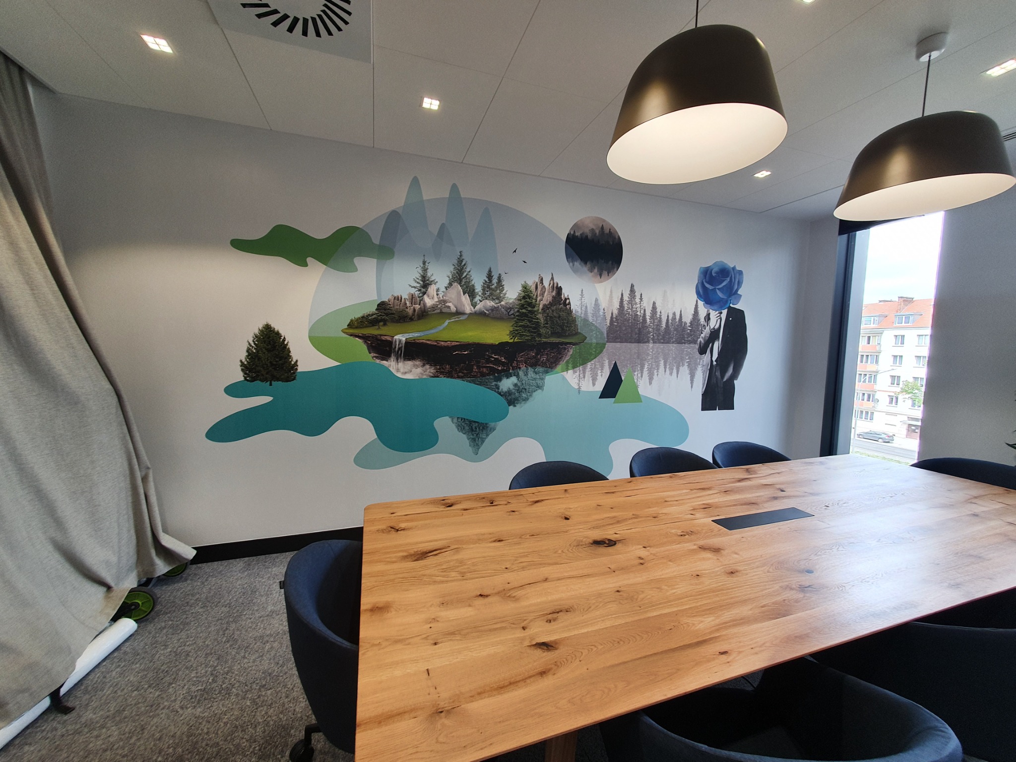 Biuro z fototapetą przedstawiającą krajobraz z wodospadem i wyspą, nad stołem konferencyjnym wiszą dwie lampy w kształcie dzwonów.