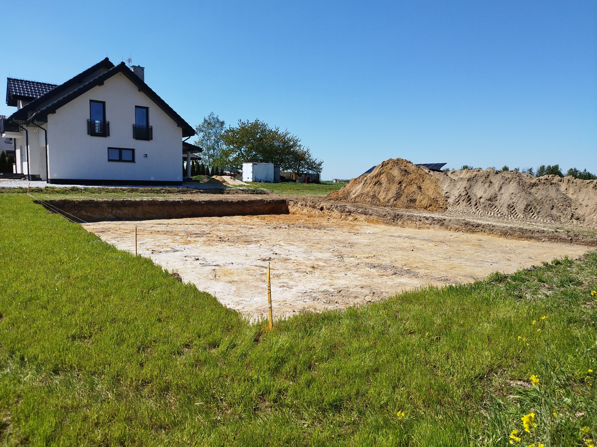 Przygotowany wykop pod fundamenty domu jednorodzinnego, widoczny zarys przyszłego budynku, kopiec ziemi w tle, słoneczny dzień.