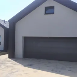 Nowoczesny dom jednorodzinny z szarą elewacją, grafitowymi elementami wykończeniowymi i bramą garażową, widok z zewnątrz w słoneczny dzień.