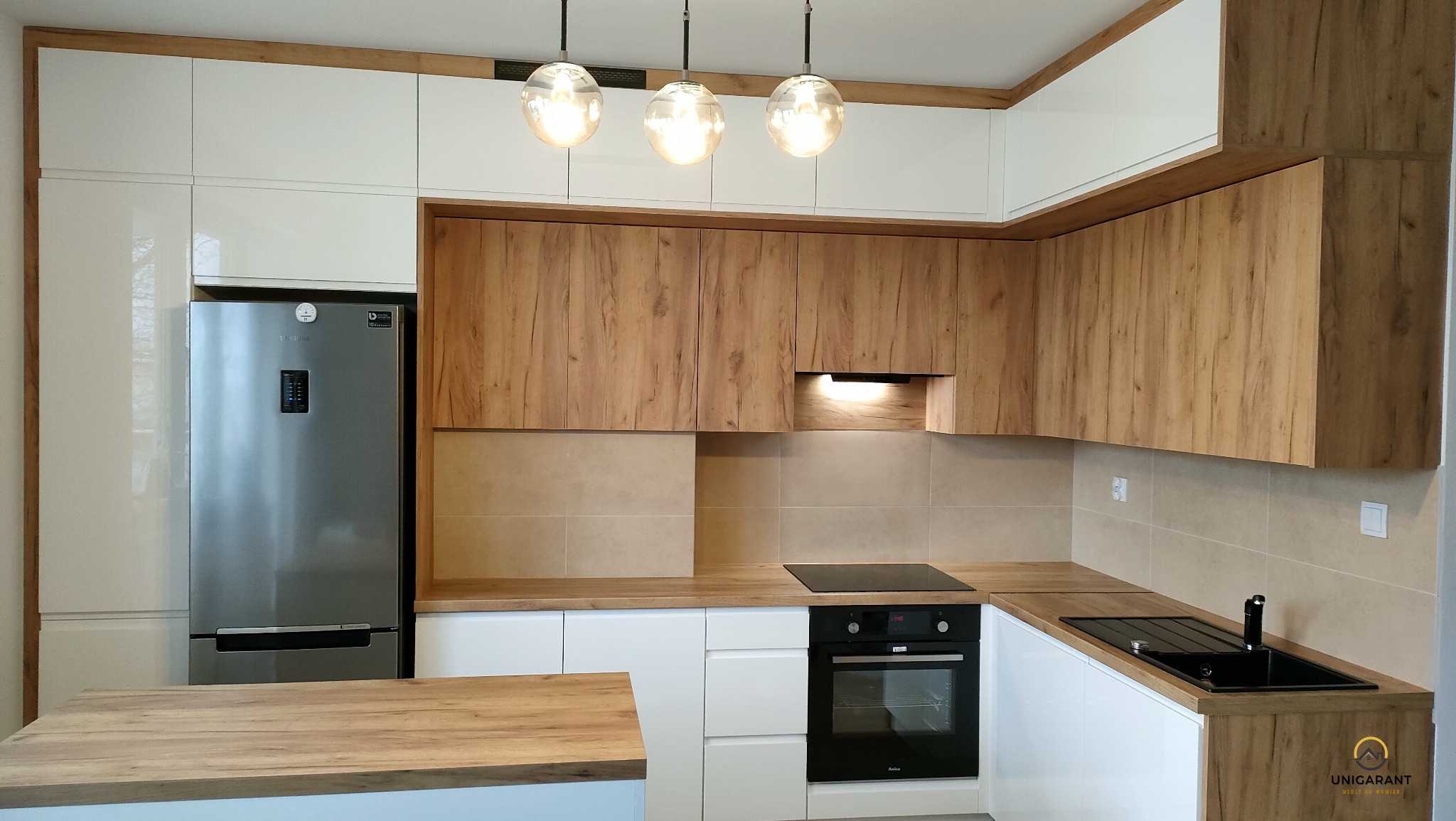 Nowoczesna kuchnia na wymiar z drewnianymi i białymi frontami, oświetleniem punktowym i srebrną lodówką Samsung.