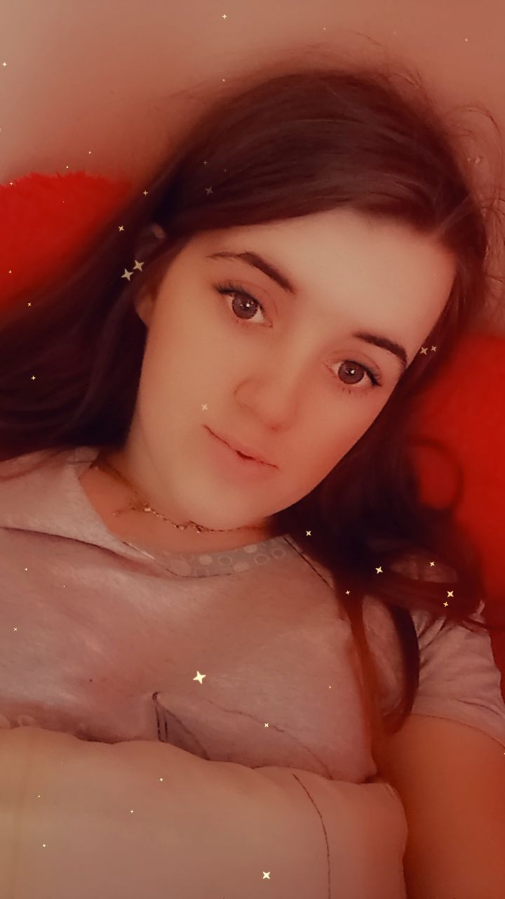 Portret młodej kobiety z długimi brązowymi włosami, delikatnym makijażem i złotym naszyjnikiem na czerwonym tle, z dodanymi efektami świetlnymi w postaci gwiazdek.