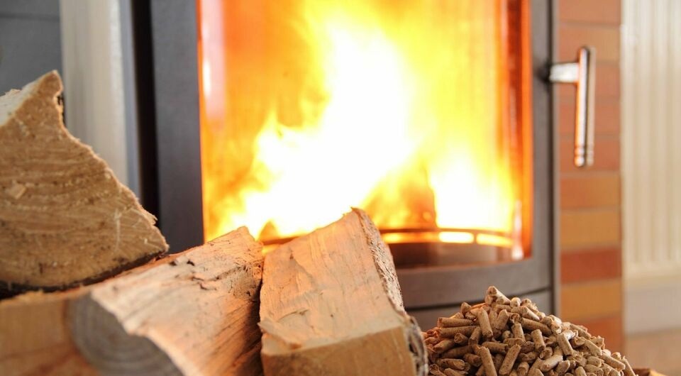 Płonący ogień w nowoczesnym piecu kominkowym, obok ułożone polana drewna i mały stos pelletu drzewnego.