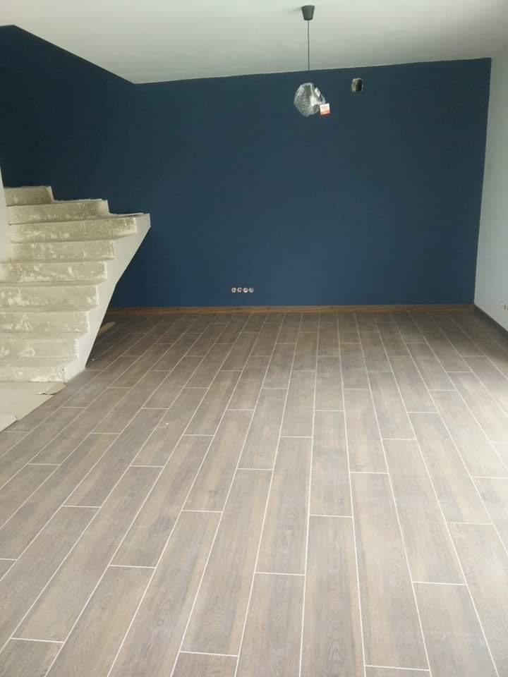Ułożona podłoga z płytek imitujących drewno w nowo wykończonym pomieszczeniu z pomalowaną na granatowo ścianą i surowymi schodami.