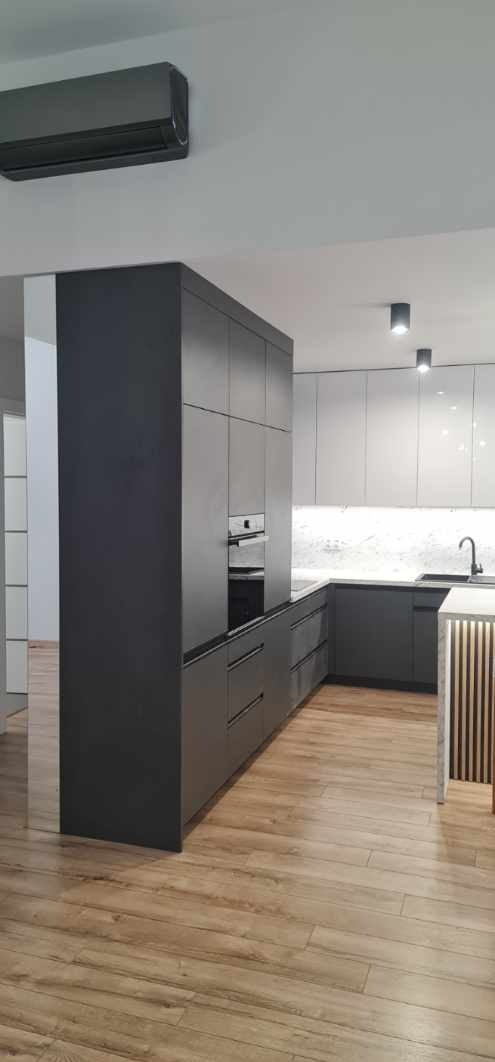 Nowoczesna kuchnia: zabudowa w odcieniach szarości z wbudowanym piekarnikiem, blatem z marmurowym wzorem i drewnianą podłogą, oświetlona punktowymi lampami sufitowymi.