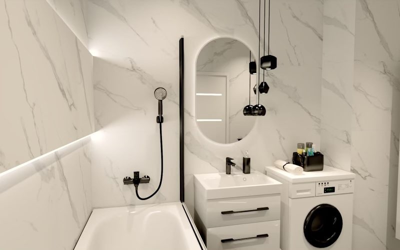 Nowoczesna łazienka z marmurowymi płytkami, owalnym lustrem podświetlanym LED, czarną armaturą i wiszącymi lampami o geometrycznych kształtach, pralka zabudowana pod blatem.