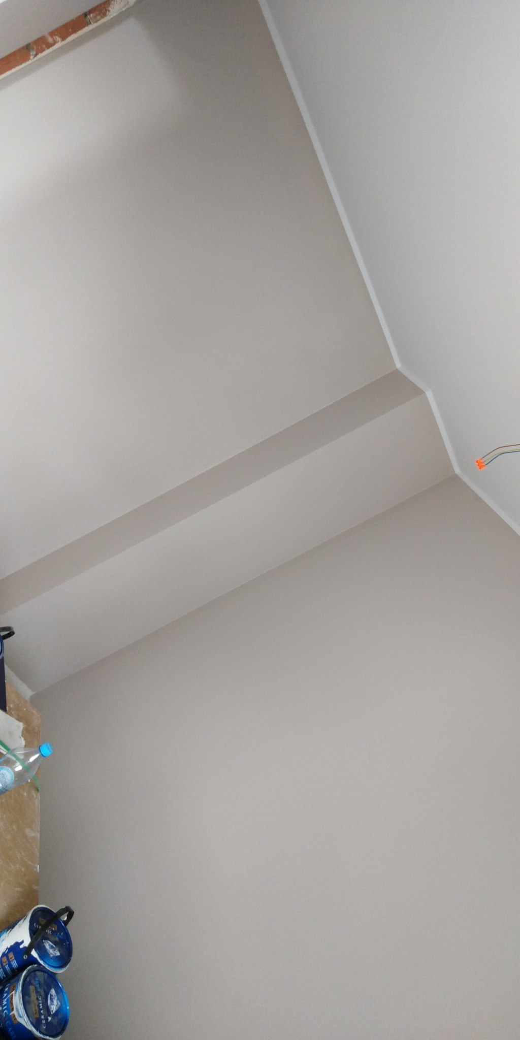 Pomieszczenie po malowaniu ścian i sufitu na jednolity, jasny odcień, z widocznymi puszkami farby w dolnym rogu.