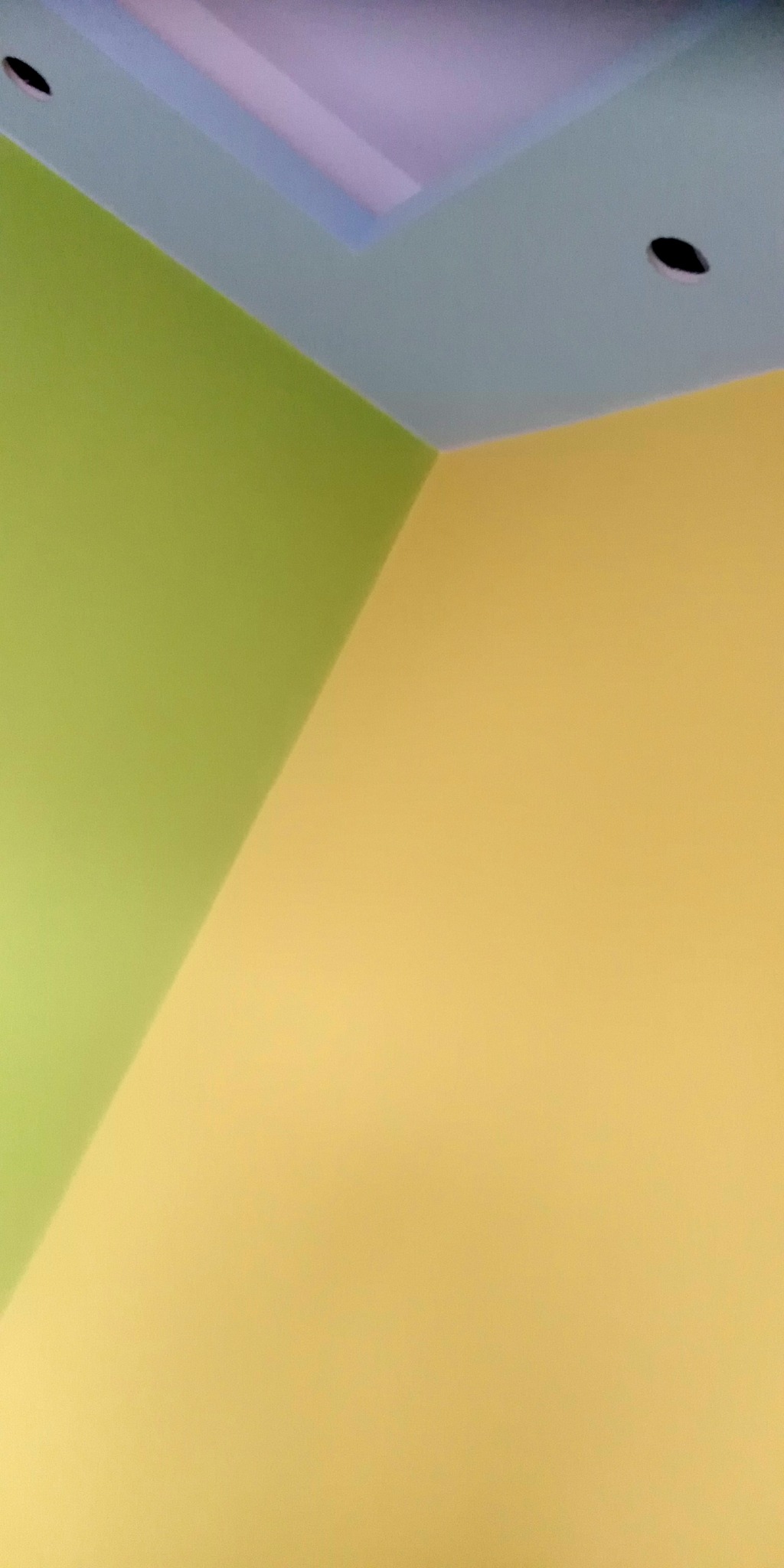 Pomieszczenie po malowaniu: ściany w odcieniach żółci i zieleni, sufit jasnoniebieski z wbudowanym oświetleniem.