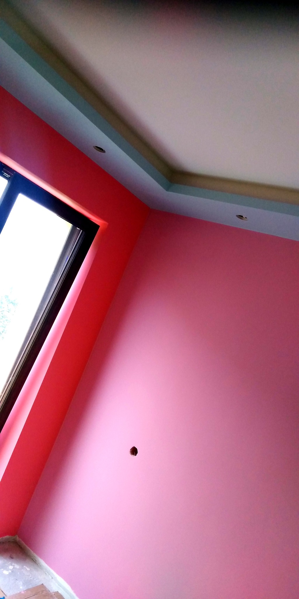 Świeżo pomalowane na różowo wnętrze pokoju z oknem i fragmentem sufitu z oświetleniem punktowym.