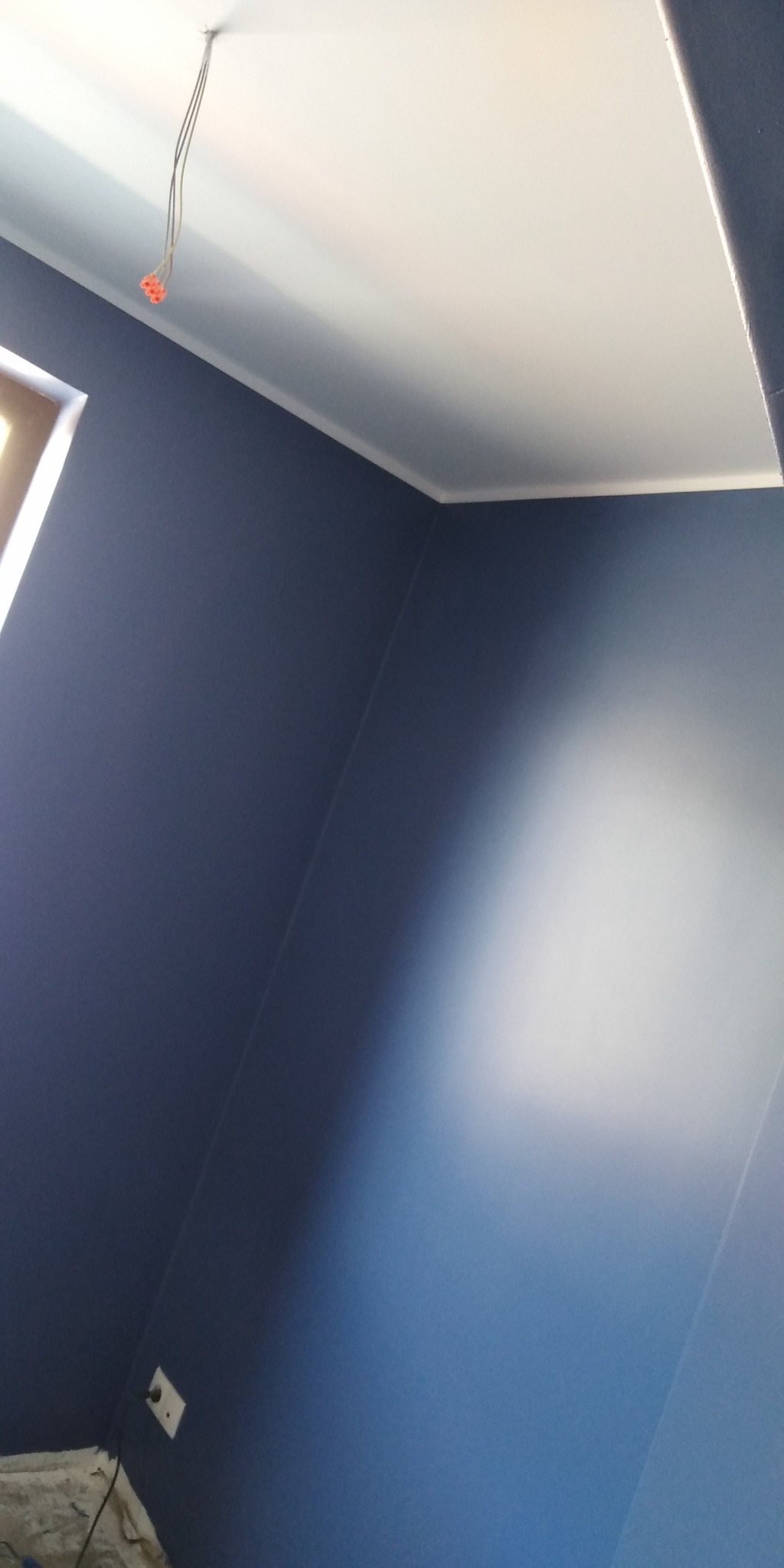 Pomieszczenie po malowaniu ścian na granatowo z białym sufitem i listwą wykończeniową; widoczne wystające przewody elektryczne.