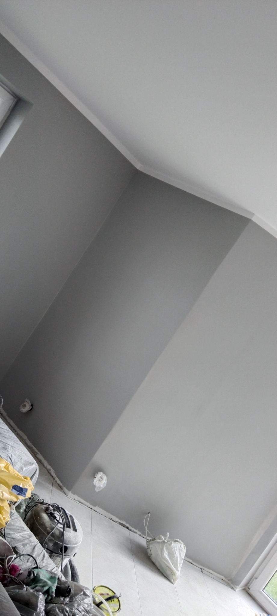 Świeżo pomalowane na szaro ściany i biały sufit w pomieszczeniu w Szczyrzycu, widoczne zabezpieczenia gniazdek elektrycznych i resztki materiałów budowlanych po remoncie.