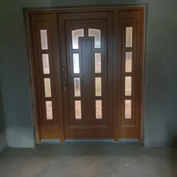 Brązowe drzwi wejściowe z szybami, otoczone surowymi szarymi ścianami i betonową podłogą w trakcie wykończenia.